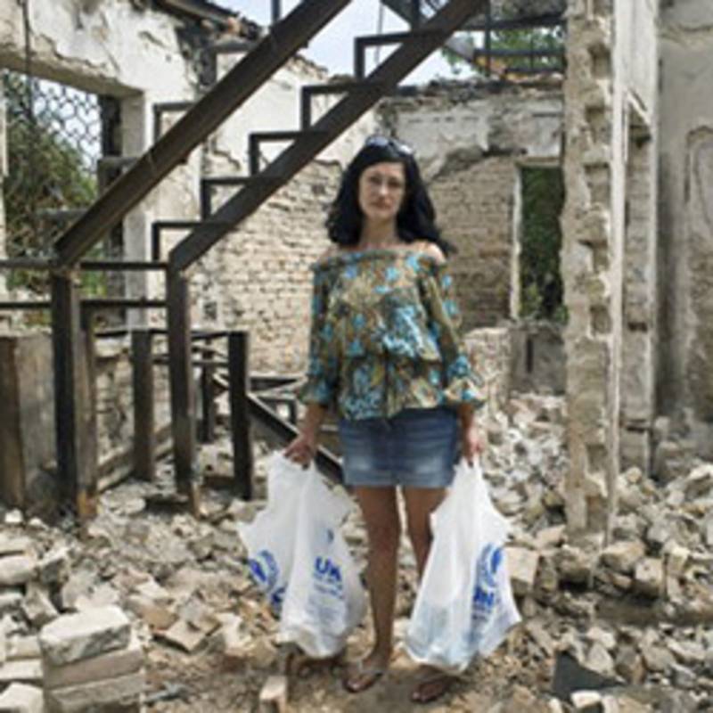 Eine Frau steht in den Ruinen ihres Hauses, nachdem sie von UNHCR Hilfsgüter erhalten hat. Foto: UNHCR